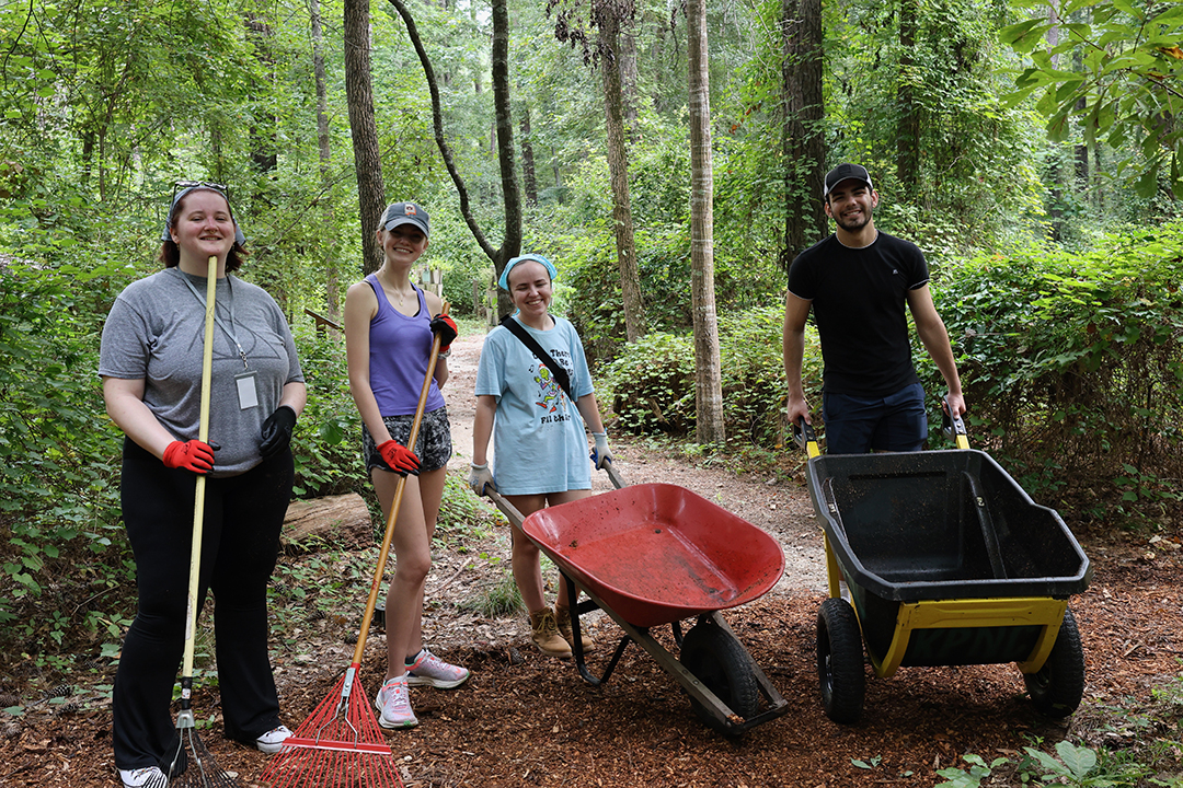four studenting in the woods with wheelbarrows and shovels in hand